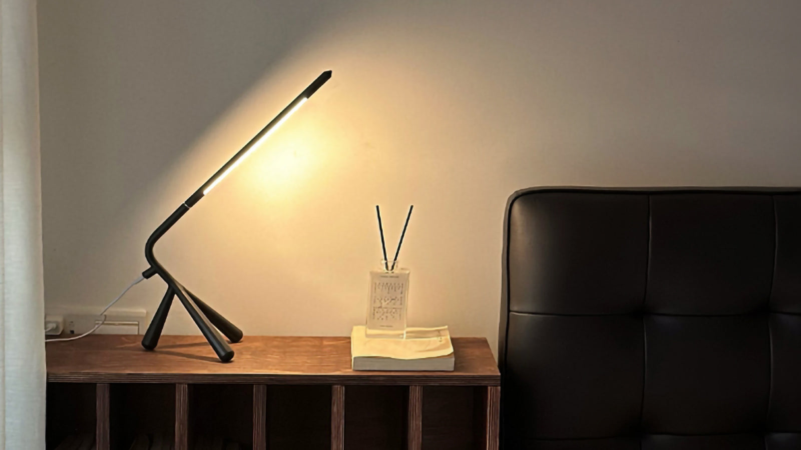 Modern black desk lamp on a wooden side table next to a black sofa.